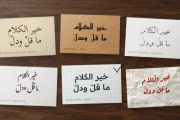 اختيار خط عربي: ست بطاقات على مكتب خشبي تحمل عبارة «خير الكلام ما قلّ ودلّ» بستة أنماط من الخطوط، وعلى إحداها علامة صح بقلم الرصاص