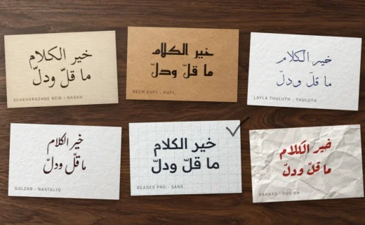 اختيار خط عربي: ست بطاقات على مكتب خشبي تحمل عبارة «خير الكلام ما قلّ ودلّ» بستة أنماط من الخطوط، وعلى إحداها علامة صح بقلم الرصاص