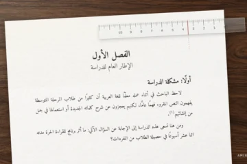 صفحة من رسالة جامعية بخط أميري بحجم 14 على مكتب خشبي، ومسطرة شفافة تقيس هامش التجليد البالغ 3.5 سم